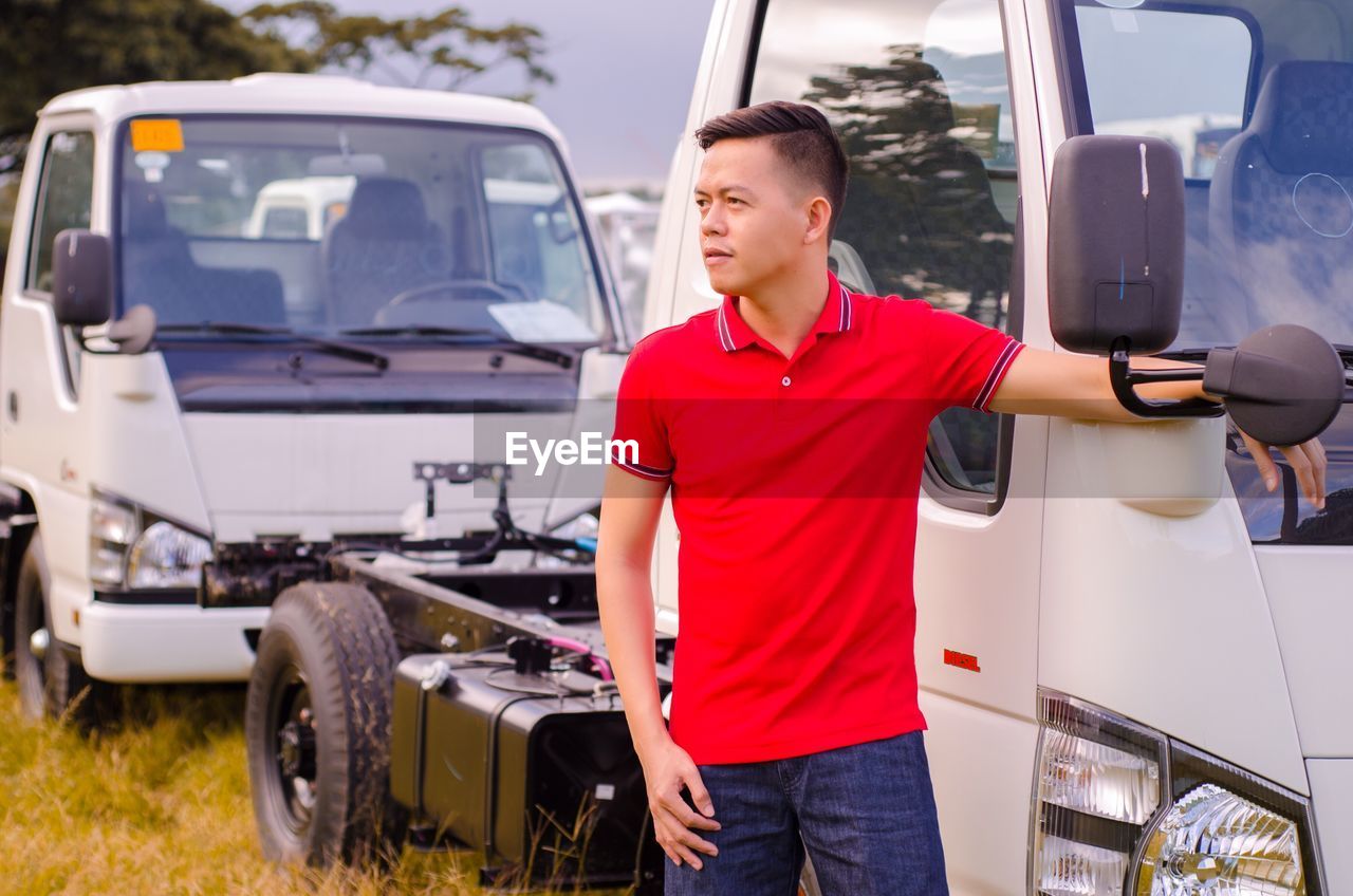 Young man standing by parked vehicle on field