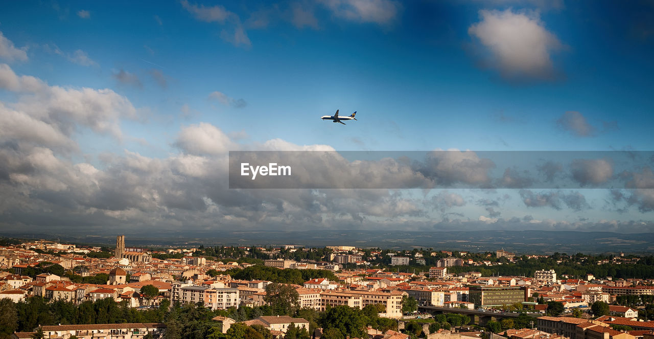 Airplane flying over cityscape against sky