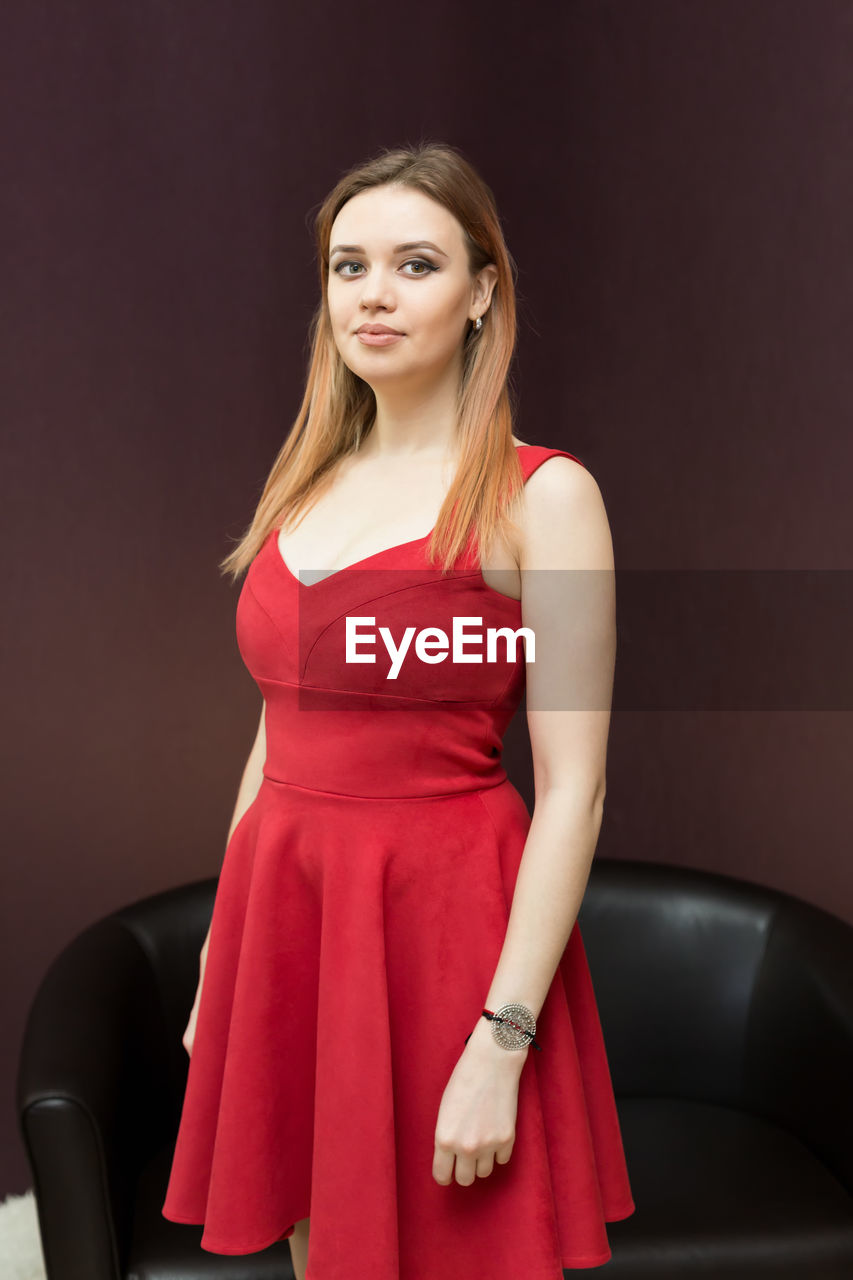 Portrait of beautiful young woman wearing red dress against wall