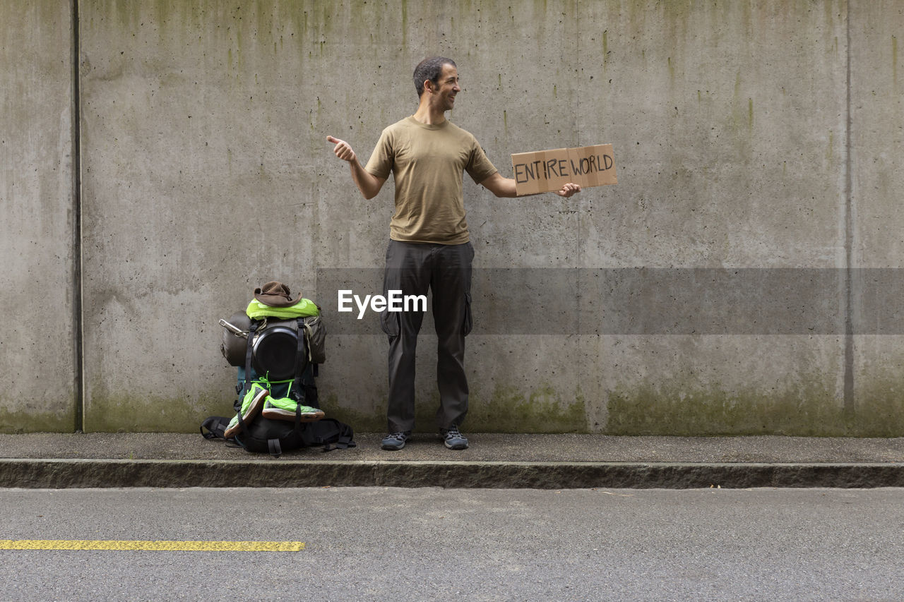 Man holding cardboard with entire world text while standing against wall 