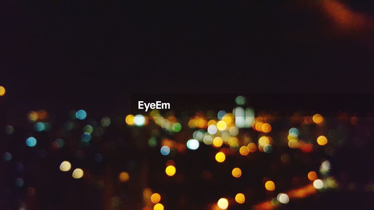 DEFOCUSED IMAGE OF ILLUMINATED CITYSCAPE AGAINST SKY