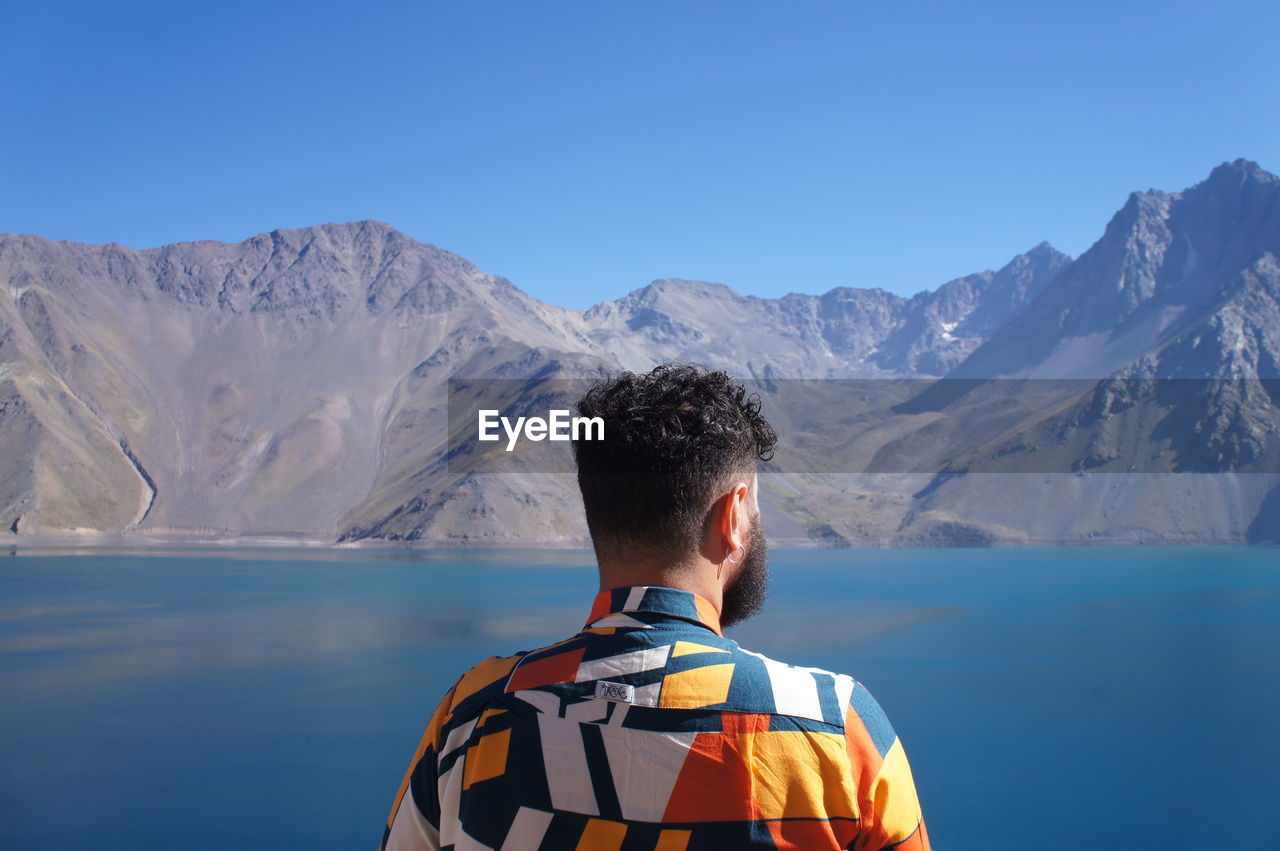 REAR VIEW OF MAN LOOKING AT MOUNTAINS AGAINST SKY