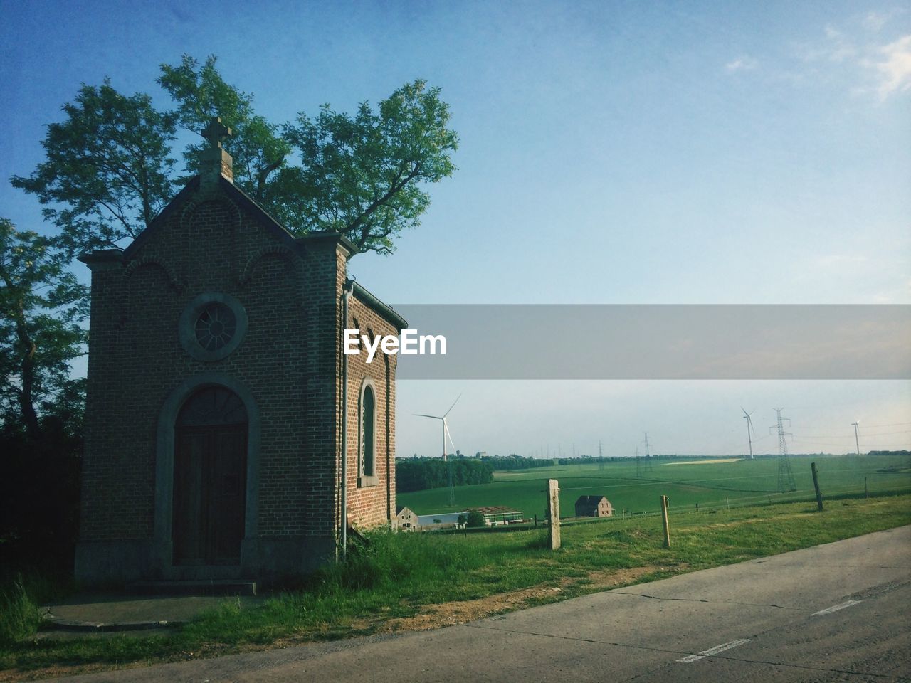 Small chapel on the side of a road with modern wind mill and field