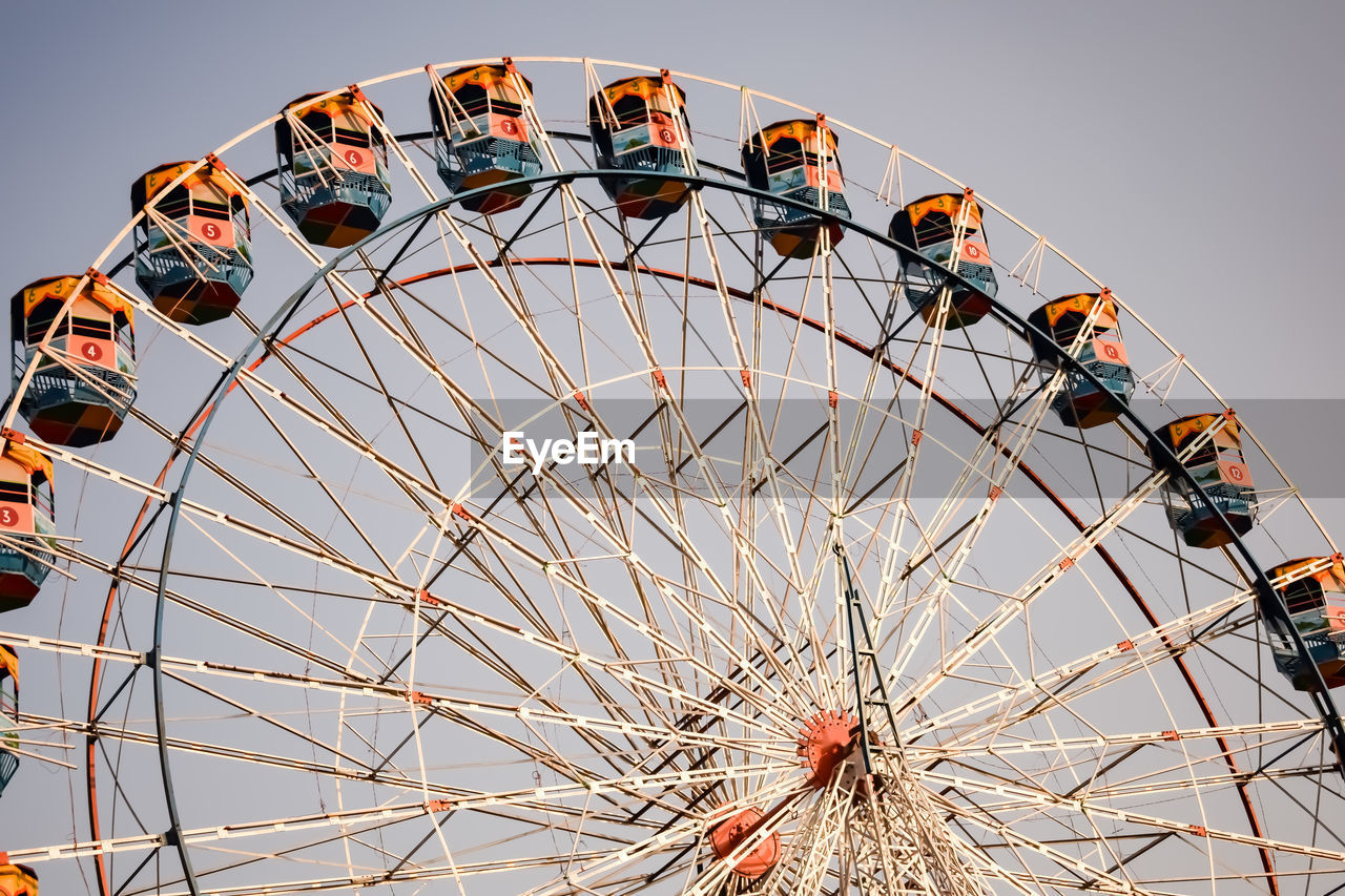 ferris wheel, amusement park ride, amusement park, arts culture and entertainment, carnival, leisure activity, traveling carnival, fun, sky, circle, nature, geometric shape, recreation, enjoyment, amber, wheel, no people, grey, travel destinations, shape, multi colored, large, outdoors, architecture, amusement ride, park, spinning, spoke, clear sky, day, holiday, low angle view