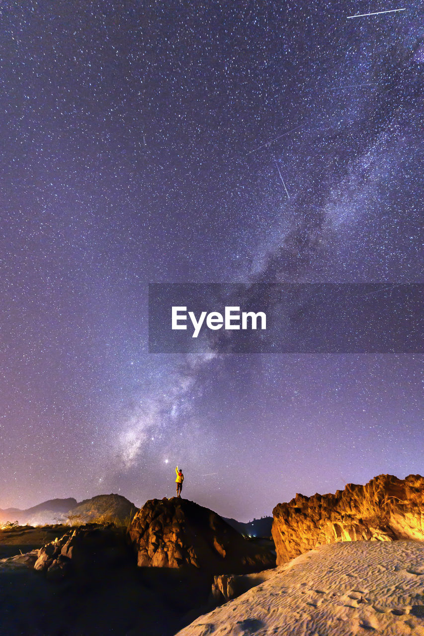 Rear view of man standing on rocks against sky at night