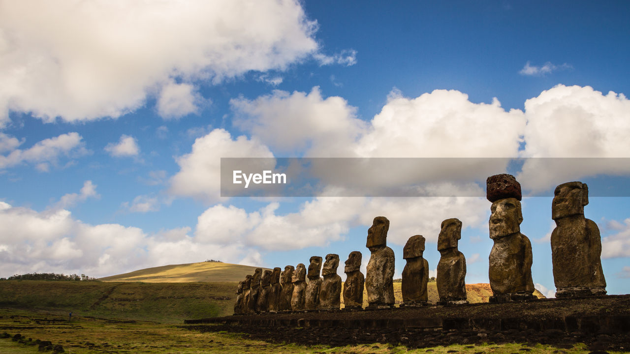 Ancient statues on field against sky