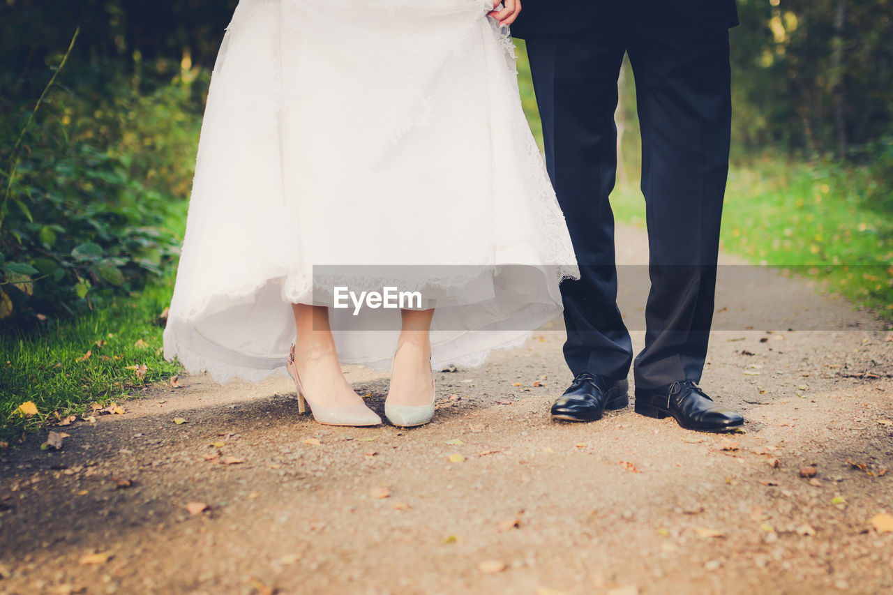 Low section of bride and groom standing on footpath