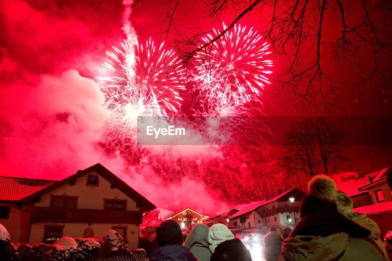 Rear view of people looking at fireworks display against sky at night