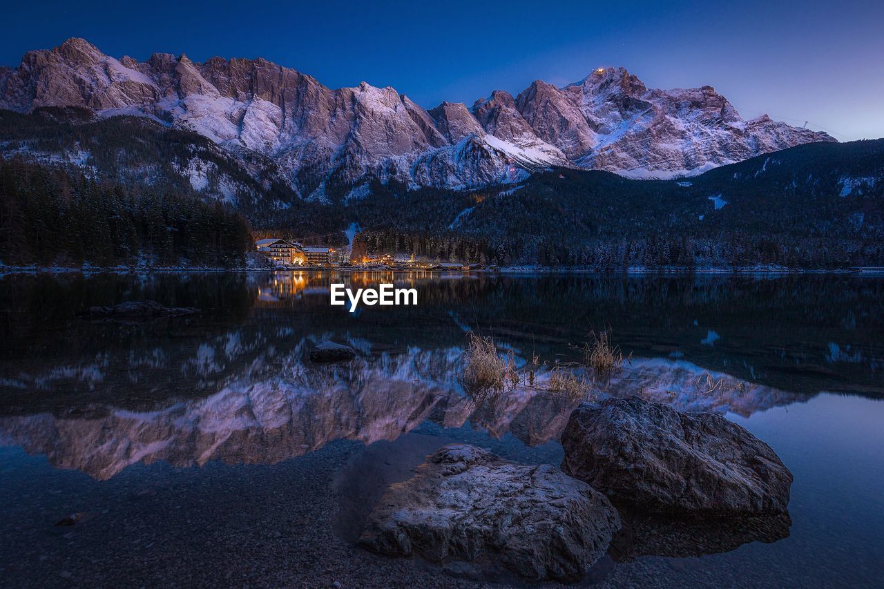 Scenic view of lake by mountains against clear sky at dusk