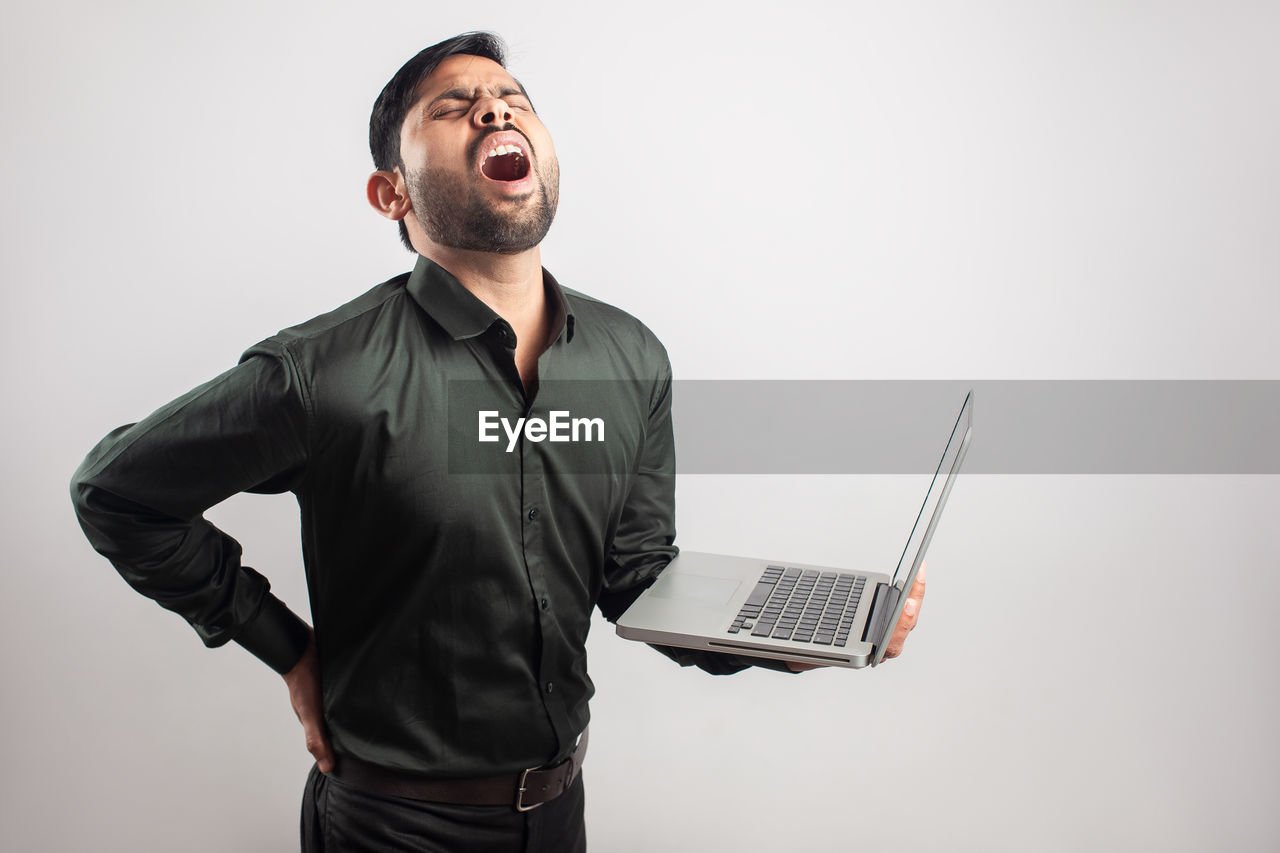 one person, technology, adult, laptop, wireless technology, computer, communication, men, using laptop, indoors, studio shot, copy space, business, emotion, happiness, person, mouth open, internet, young adult, businessman, smiling, looking, business finance and industry, cheerful, waist up, standing, computer network, portrait, clothing, occupation, portability, positive emotion, human mouth, laughing, gray