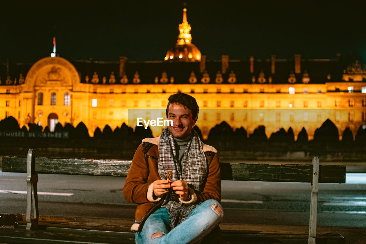 Young man sitting and eating sweets at illuminated city at night