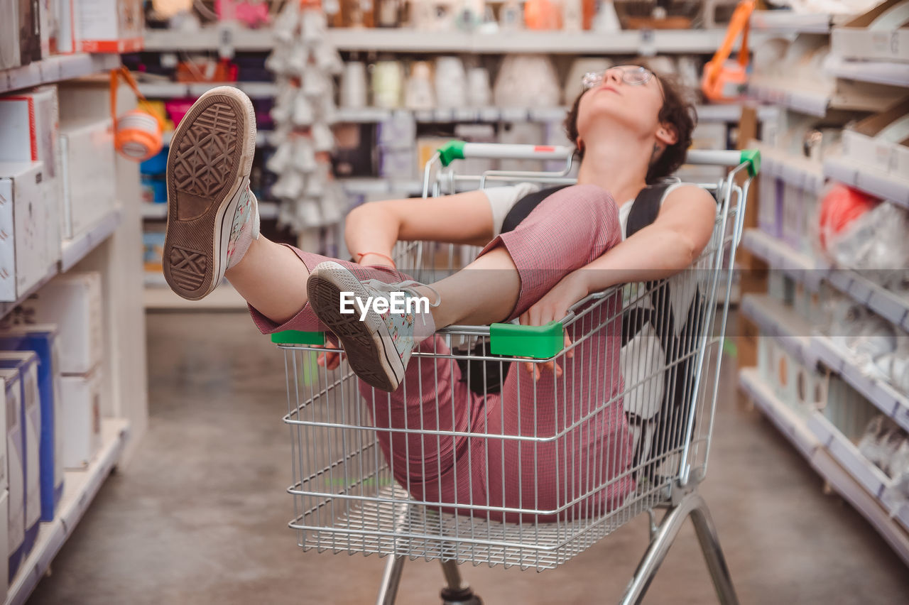 The girl is sitting in a basket in the shopping hall of the supermarket. riding in cart in store