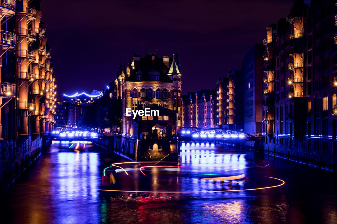 BOATS MOORED AT ILLUMINATED CITY