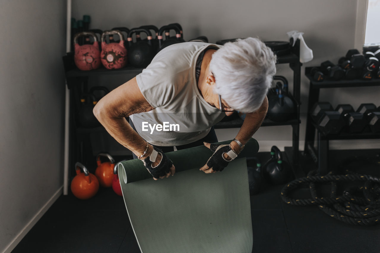 Senior woman rolling up mats after workout at gym