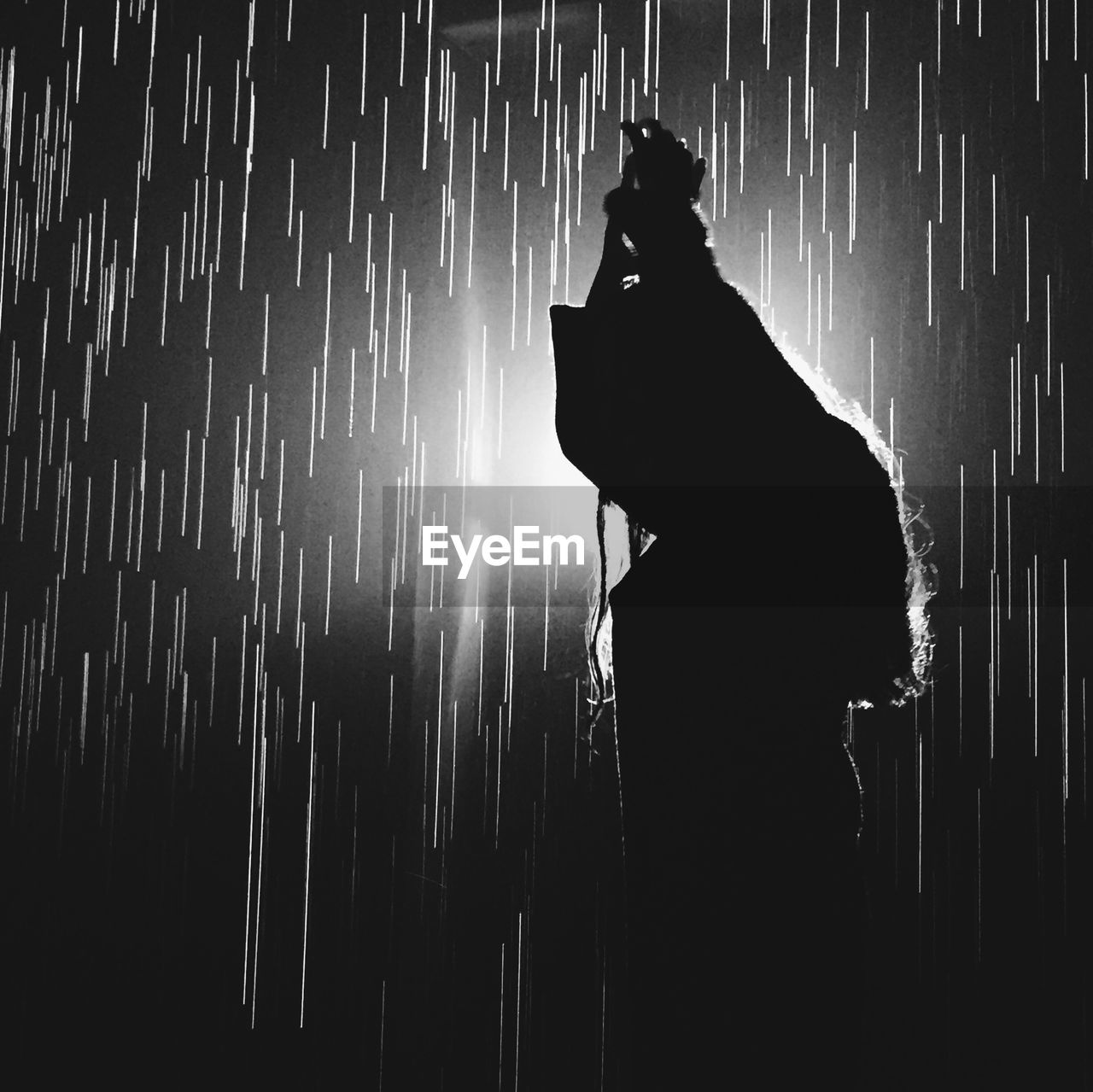 Side view of silhouette woman standing against sky at night during rainfall