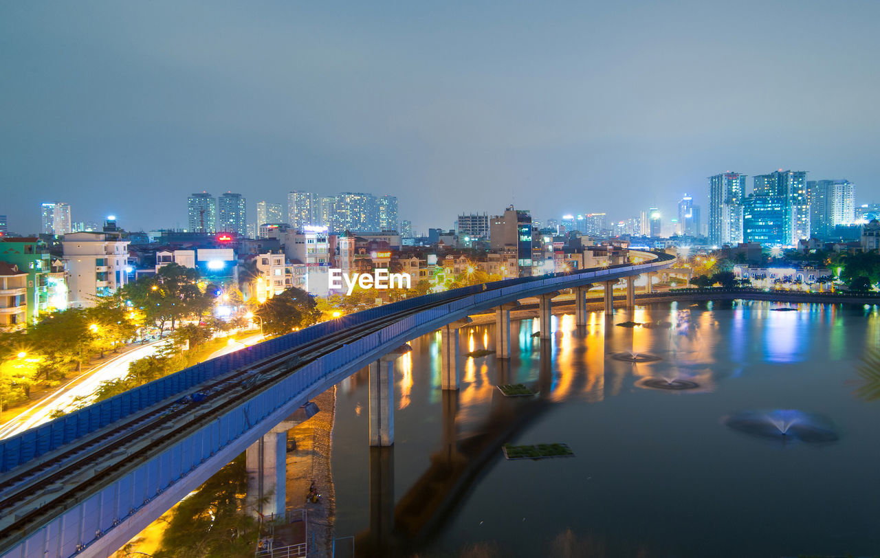 Illuminated buildings by river against sky in city at night