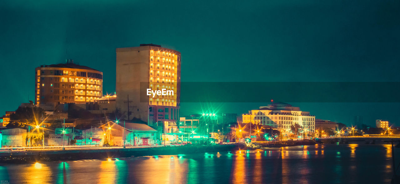 Illuminated buildings by river in city at night