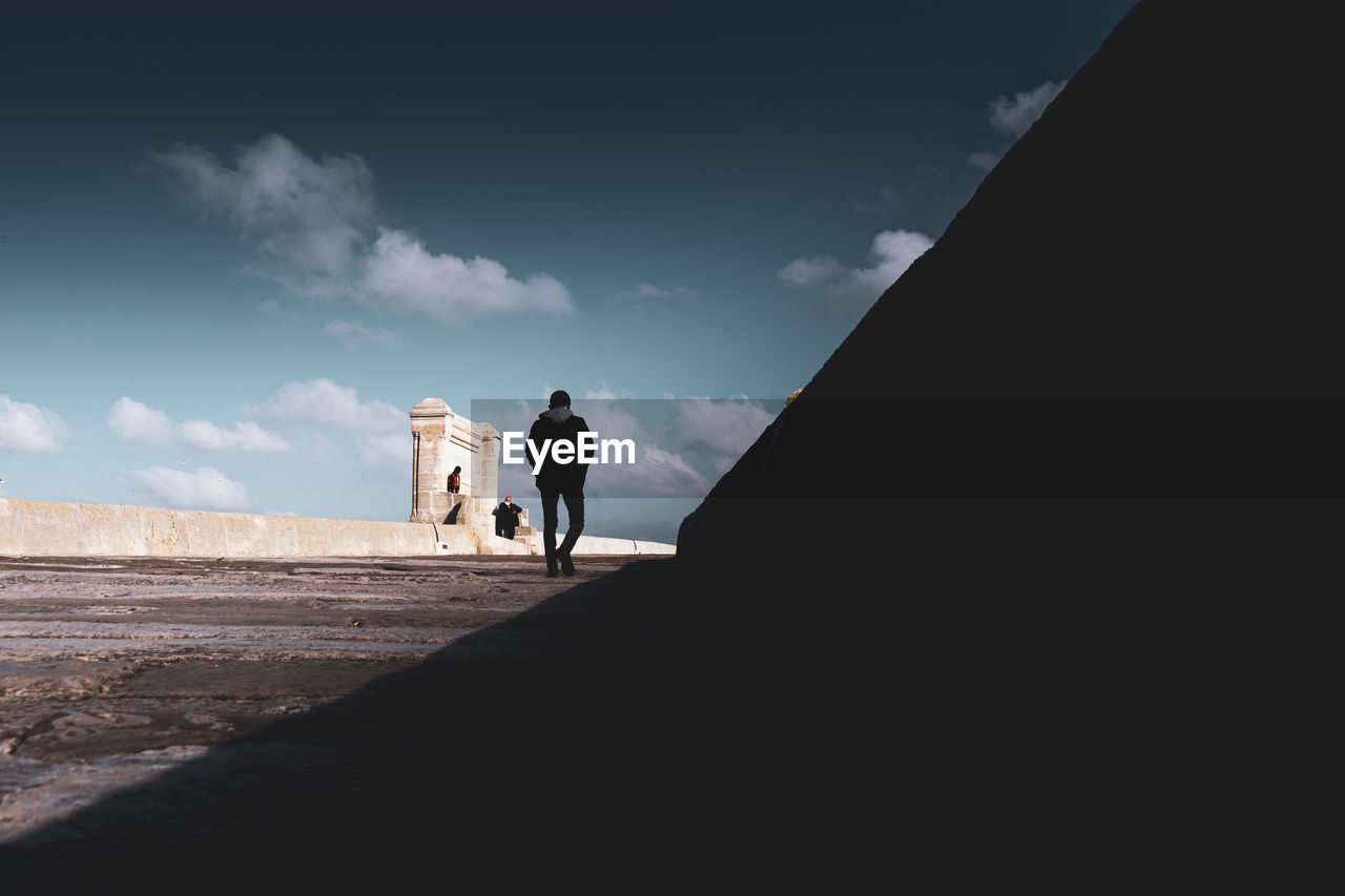 REAR VIEW OF COUPLE WALKING ON ROAD AGAINST SKY