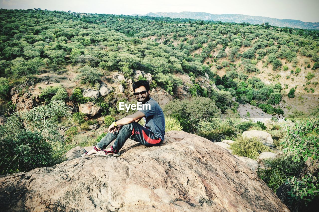 Smiling mid adult man sitting on rock over landscape