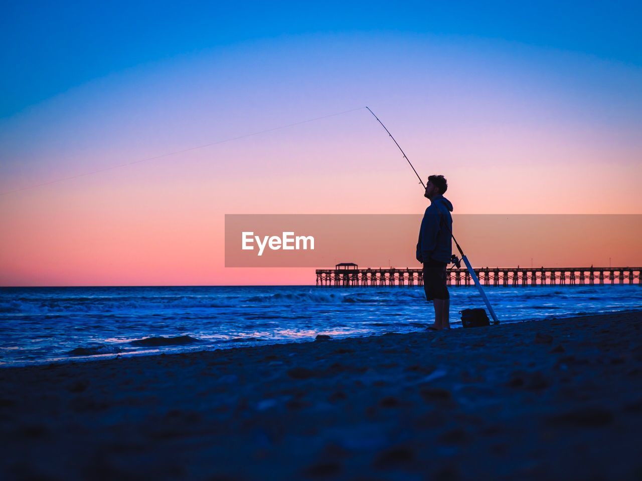 Surface level view of silhouette man fishing on shore against clear sky