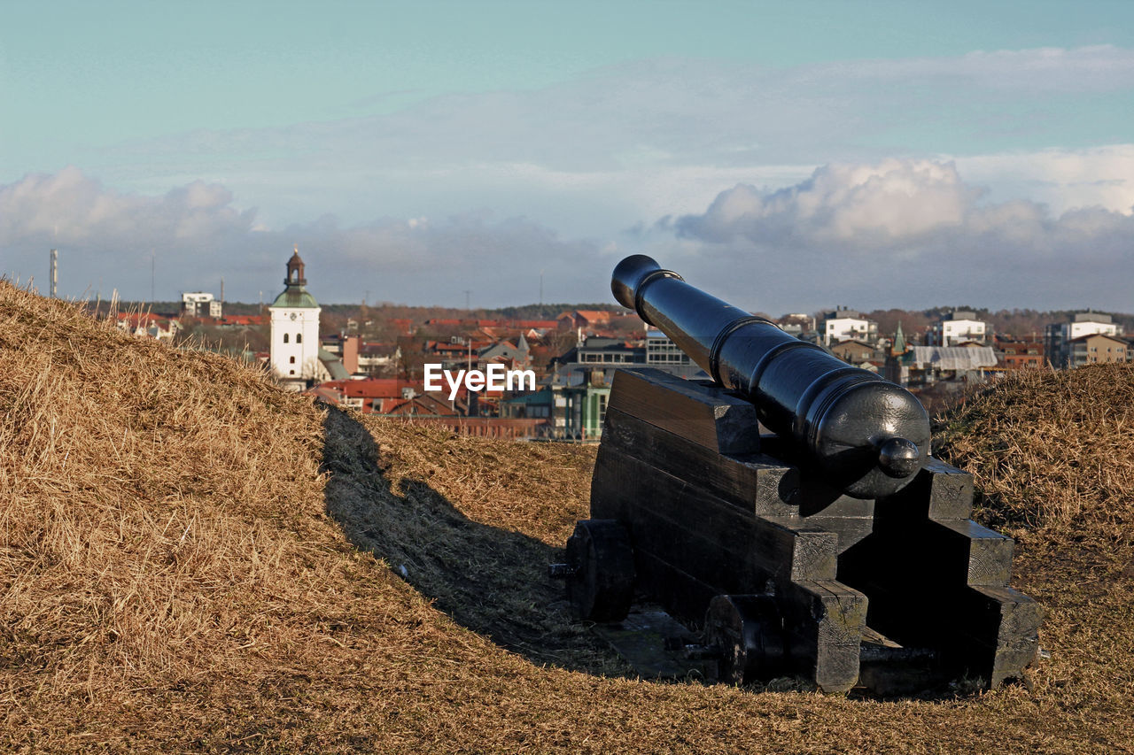 Cannon to buildings on field against sky