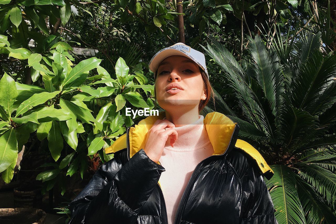 Portrait of young woman standing against plants