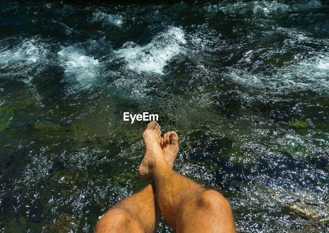 Low section of man dangling legs over lake