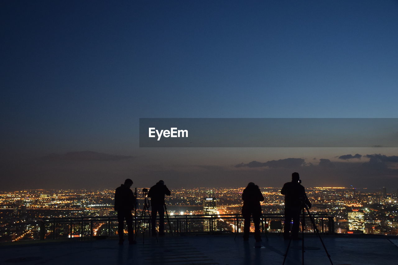 Silhouette people on terrace overlooking illuminated cityscape at dusk