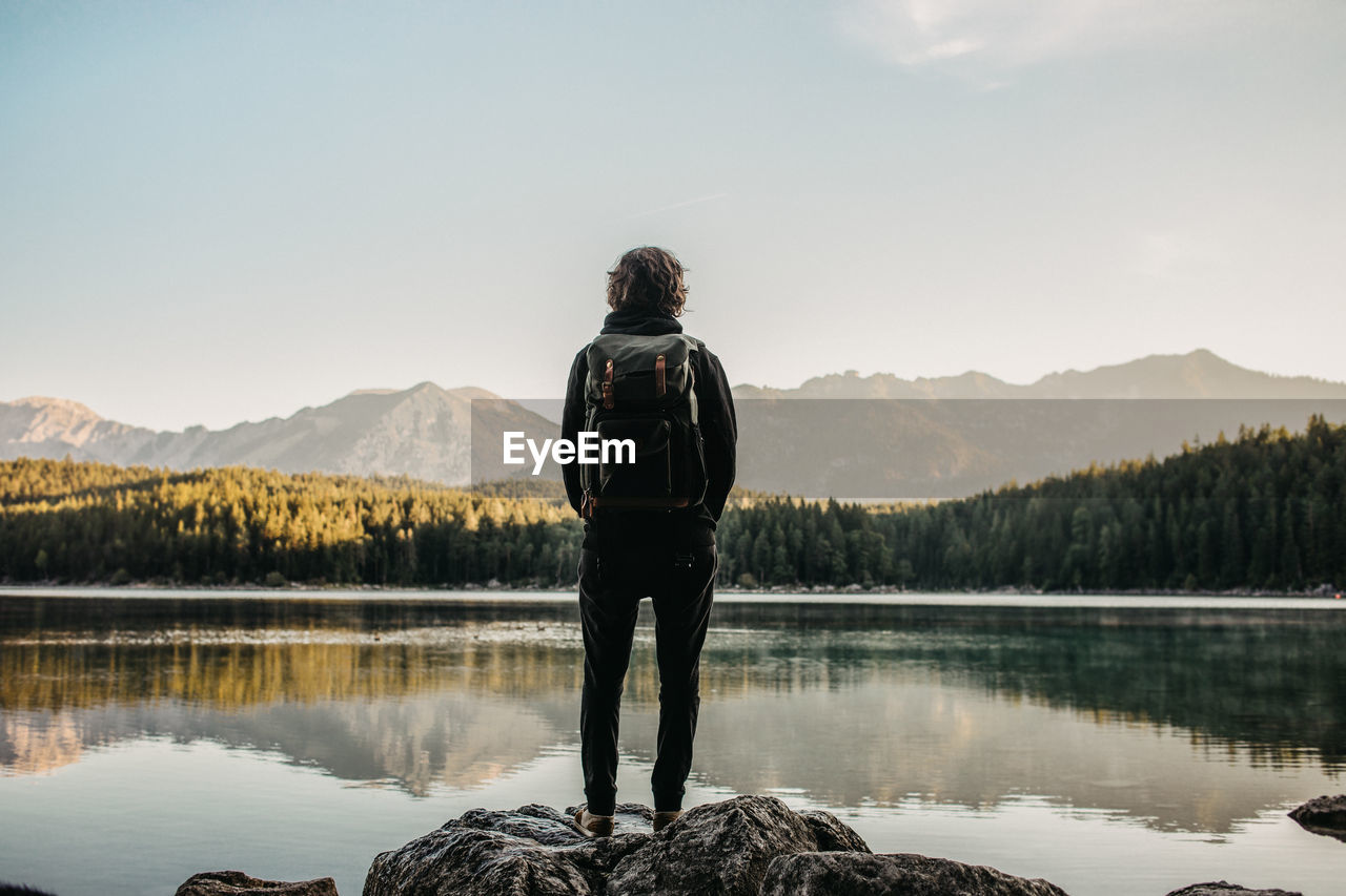 Rear view of person with backpack standing by lake against sky