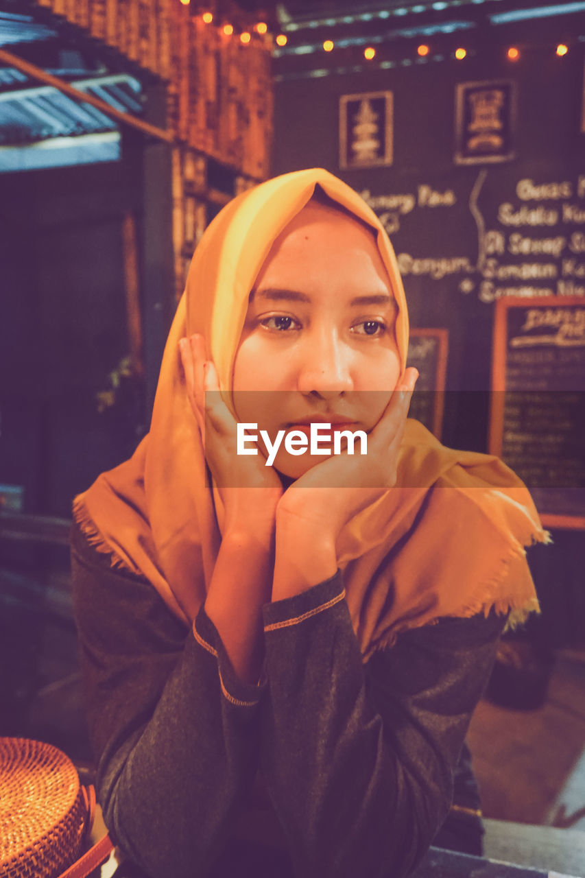 Woman with hand on chin sitting in restaurant at night