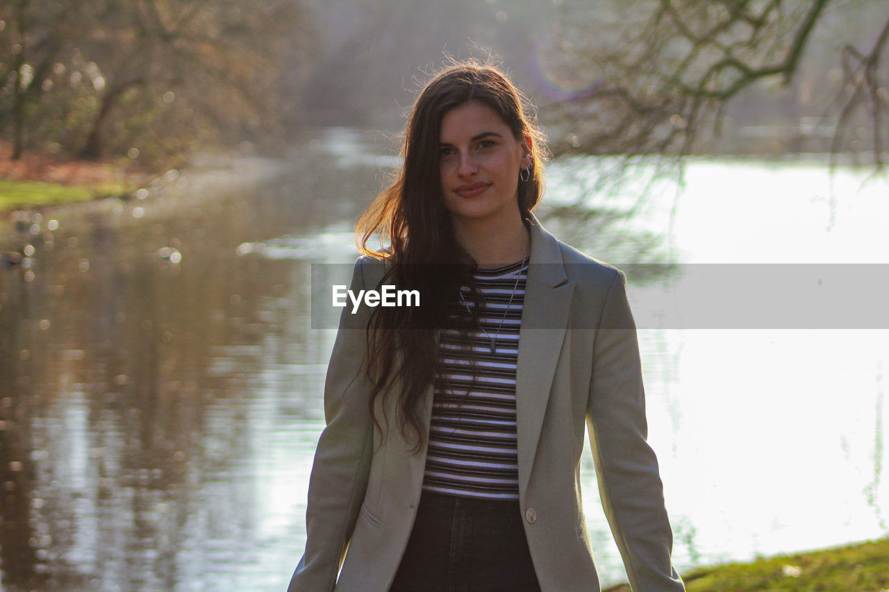 Portrait of beautiful young woman standing outdoors in front of lake