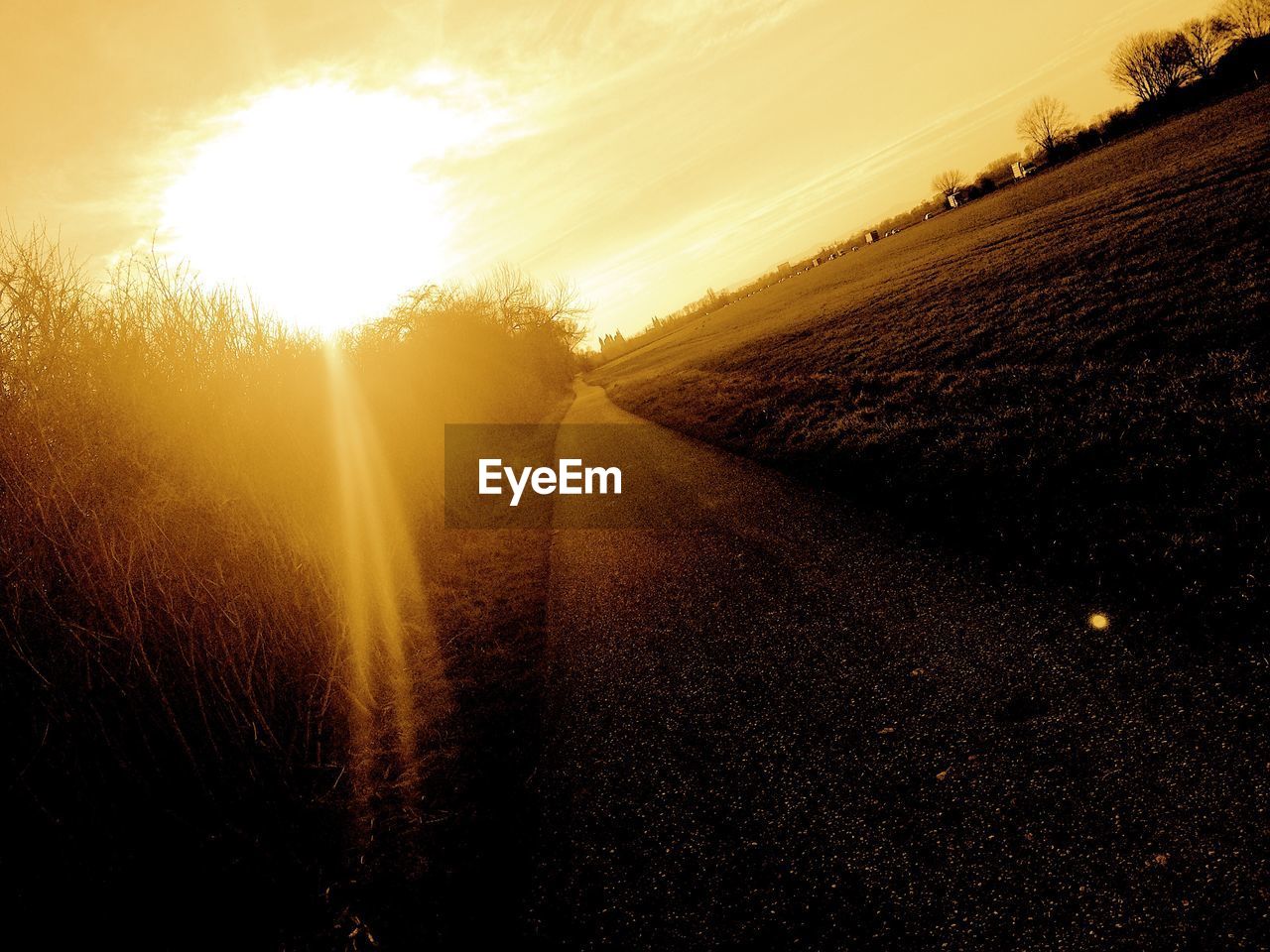 ROAD AMIDST FIELD AGAINST SKY AT SUNSET