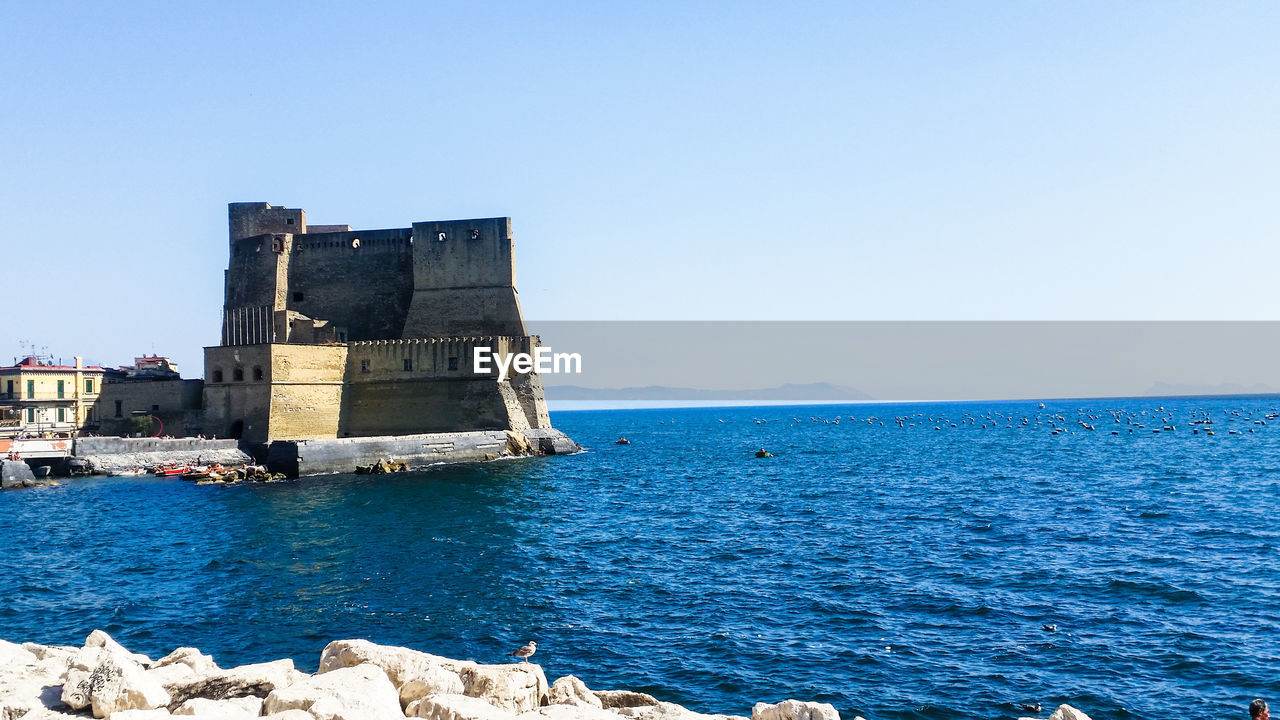 Historical building by sea against clear blue sky