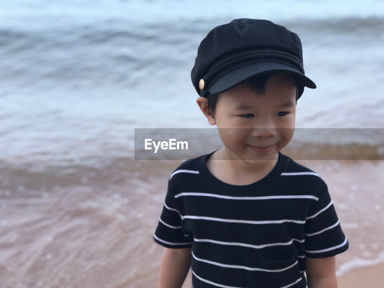 Cute smiling boy wearing cap while looking away at beach