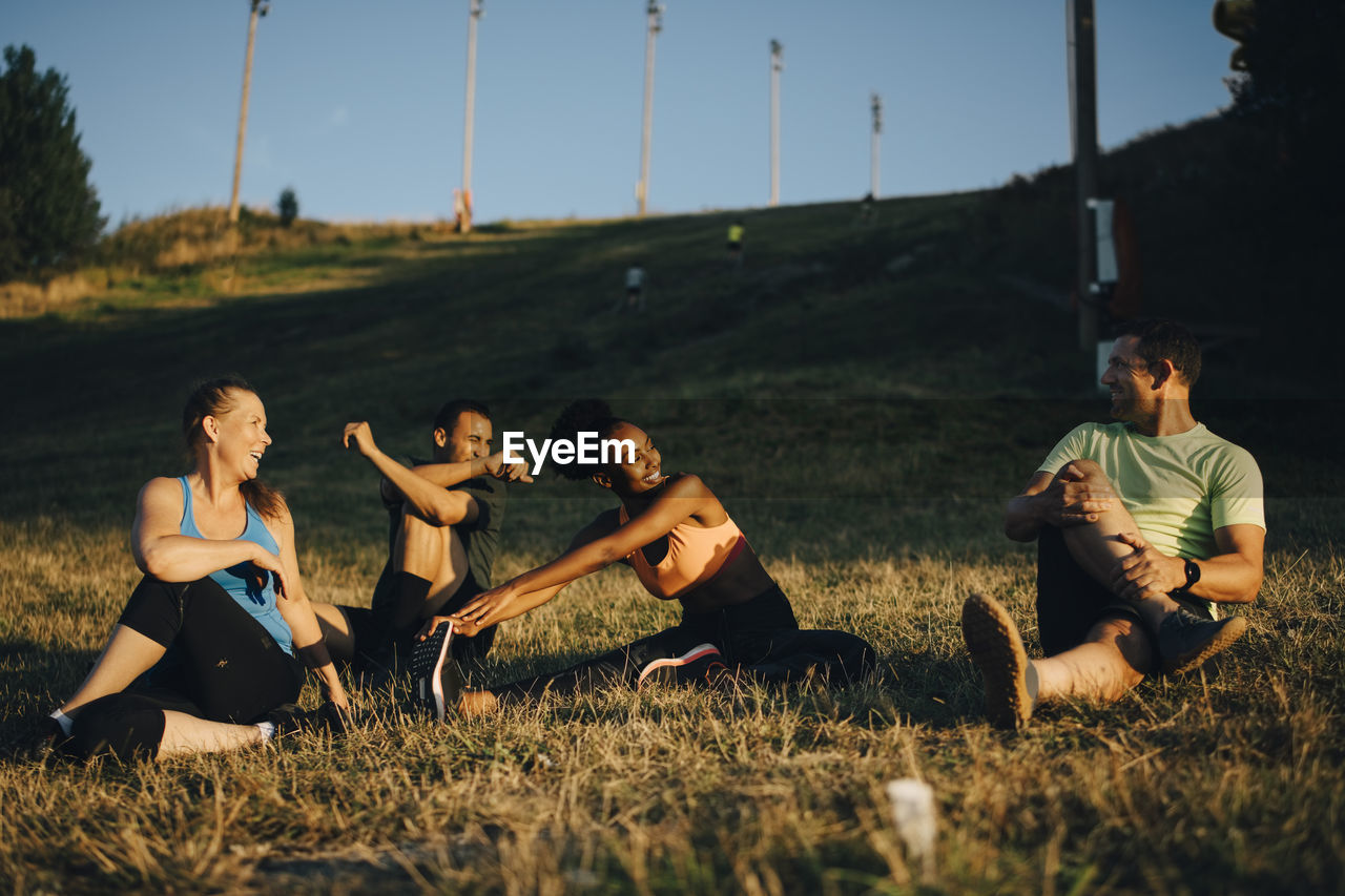 Happy male and female athletes doing stretching exercise on land during sunset