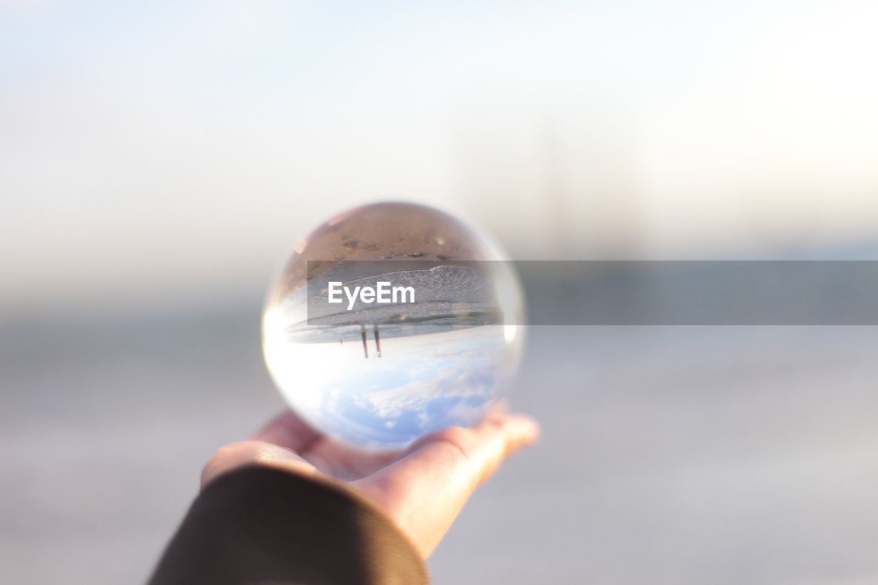 Cropped hand holding crystal ball with reflection of beach