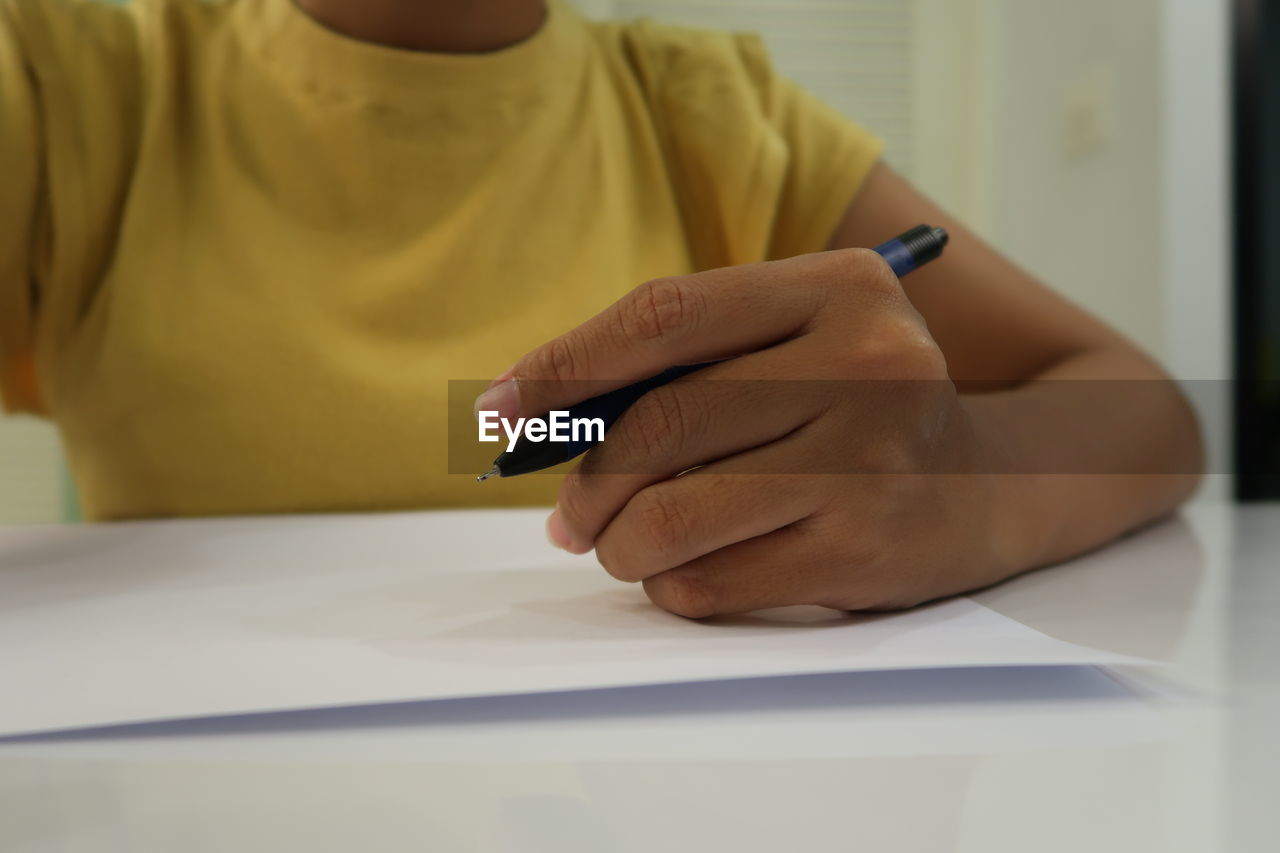 Midsection of woman holding pen on table