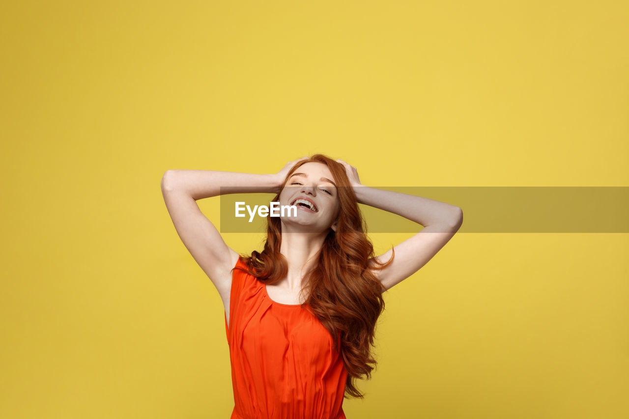 Young woman standing against yellow background