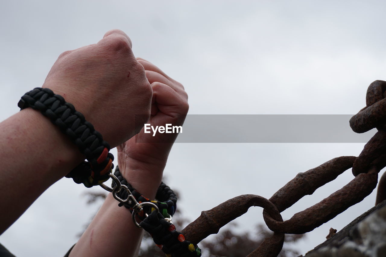 Cropped hands attached with metallic chain against sky