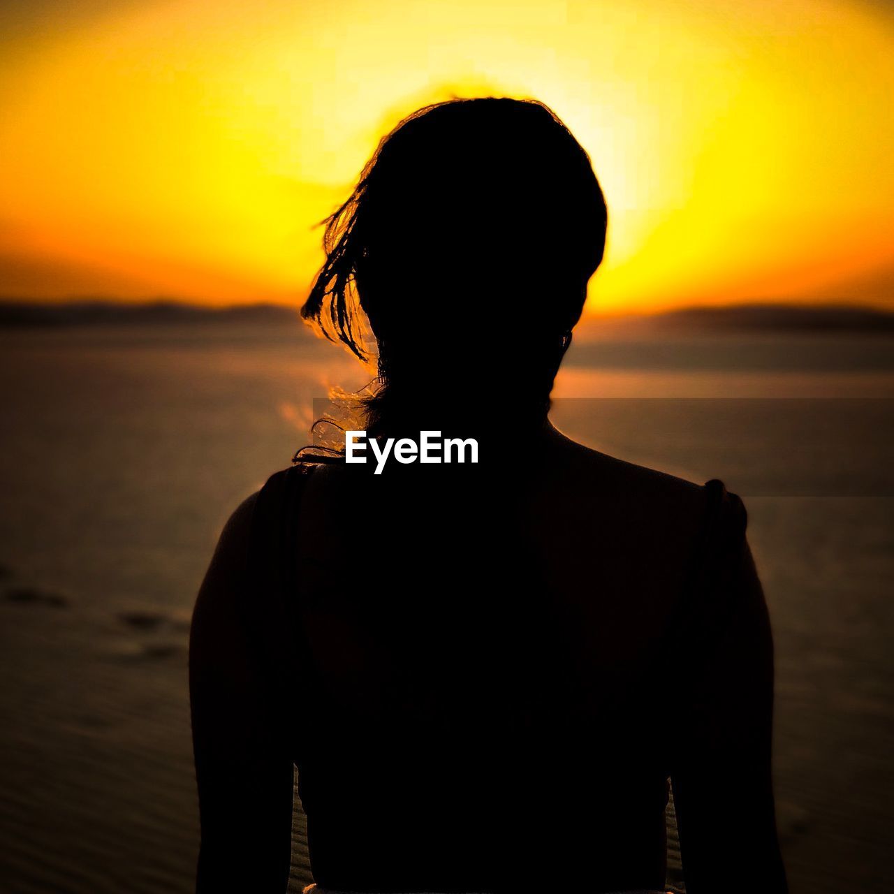 Rear view of silhouette woman standing at beach against sky during sunset