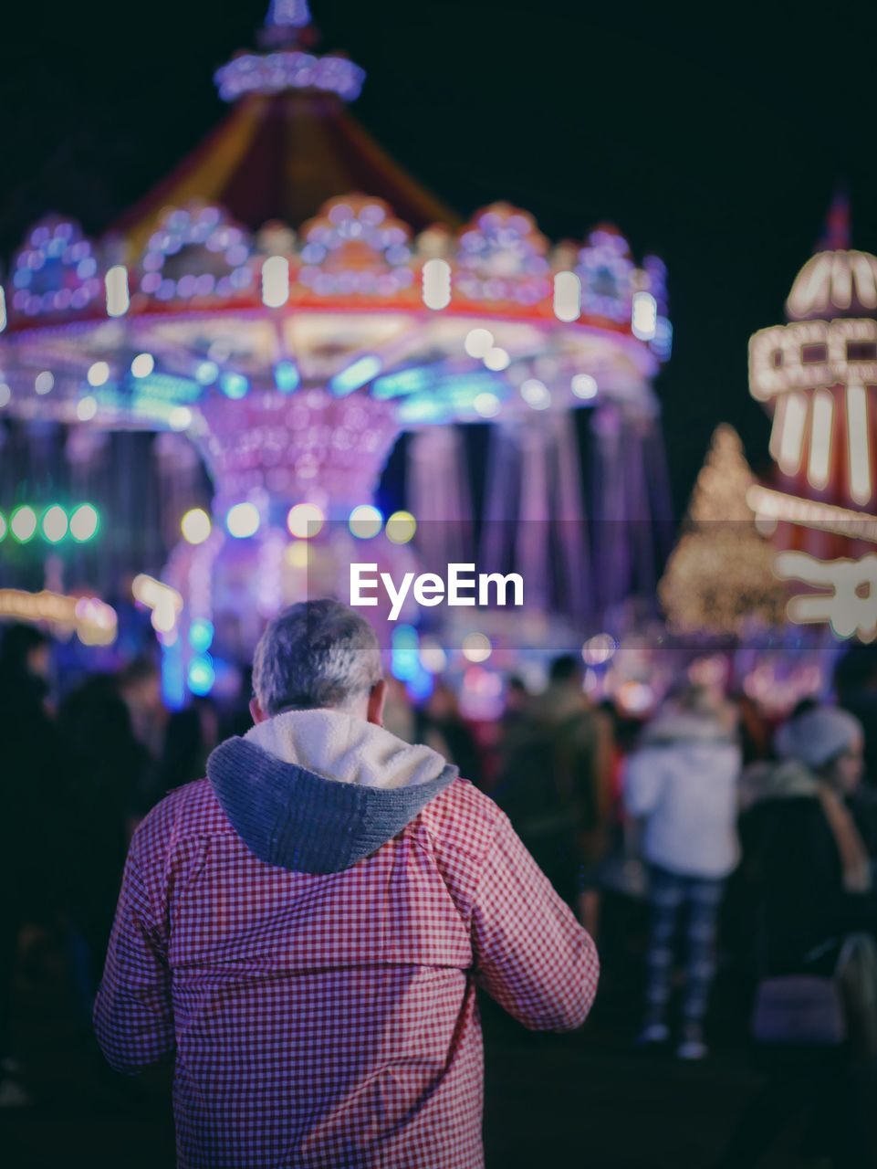 REAR VIEW OF PEOPLE AT ILLUMINATED AMUSEMENT PARK