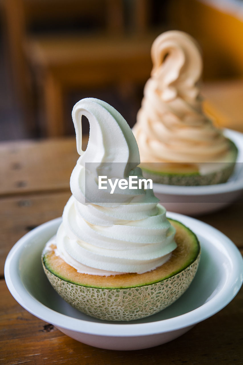 Close-up of cantaloupes with whipped creams in bowls on table