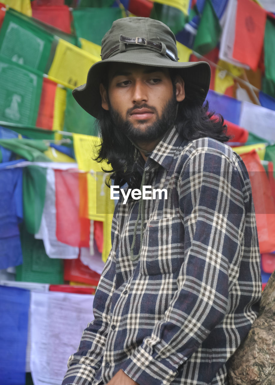 A good looking male tourist looking sideways while posing against buddhist prayer flags 