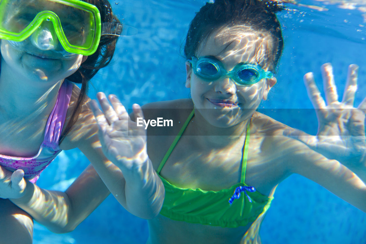 Portrait of sisters underwater in swimming pool