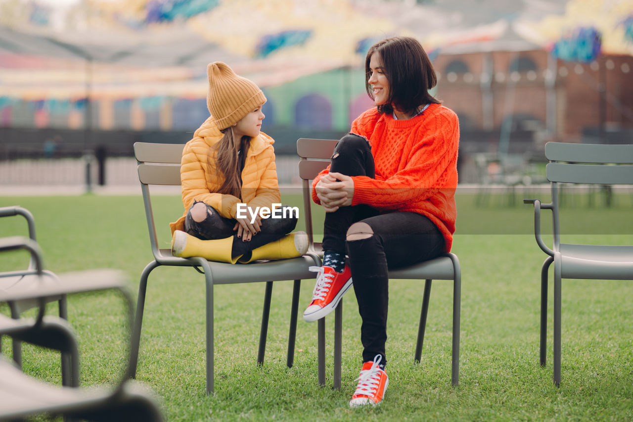 Mother talking with daughter while sitting on chairs in park