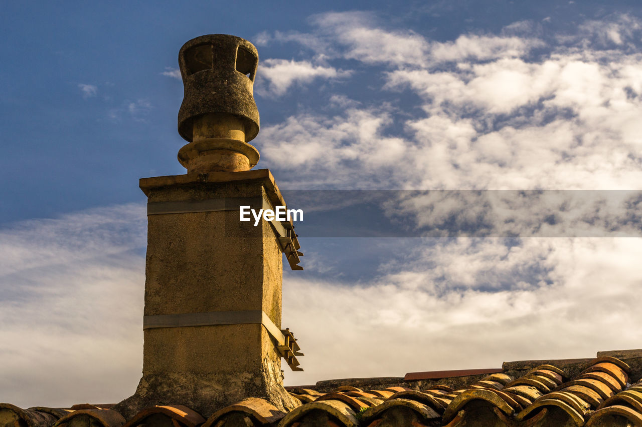 Low angle view of smoke stack on roof against cloudy sky