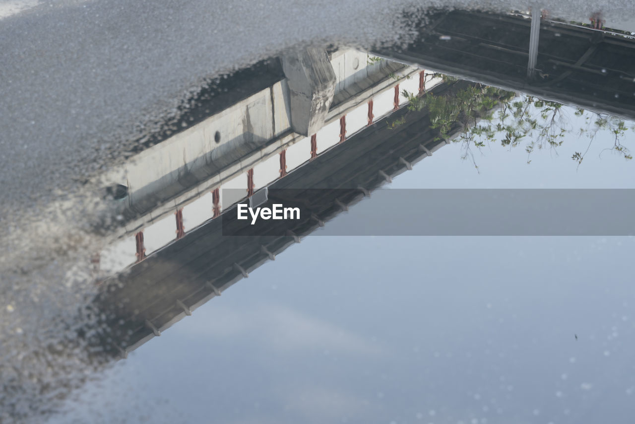 REFLECTION OF BRIDGE IN PUDDLE ON ROAD AGAINST SKY