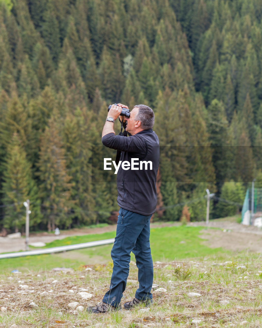 Side view of mature man looking through binoculars in forest