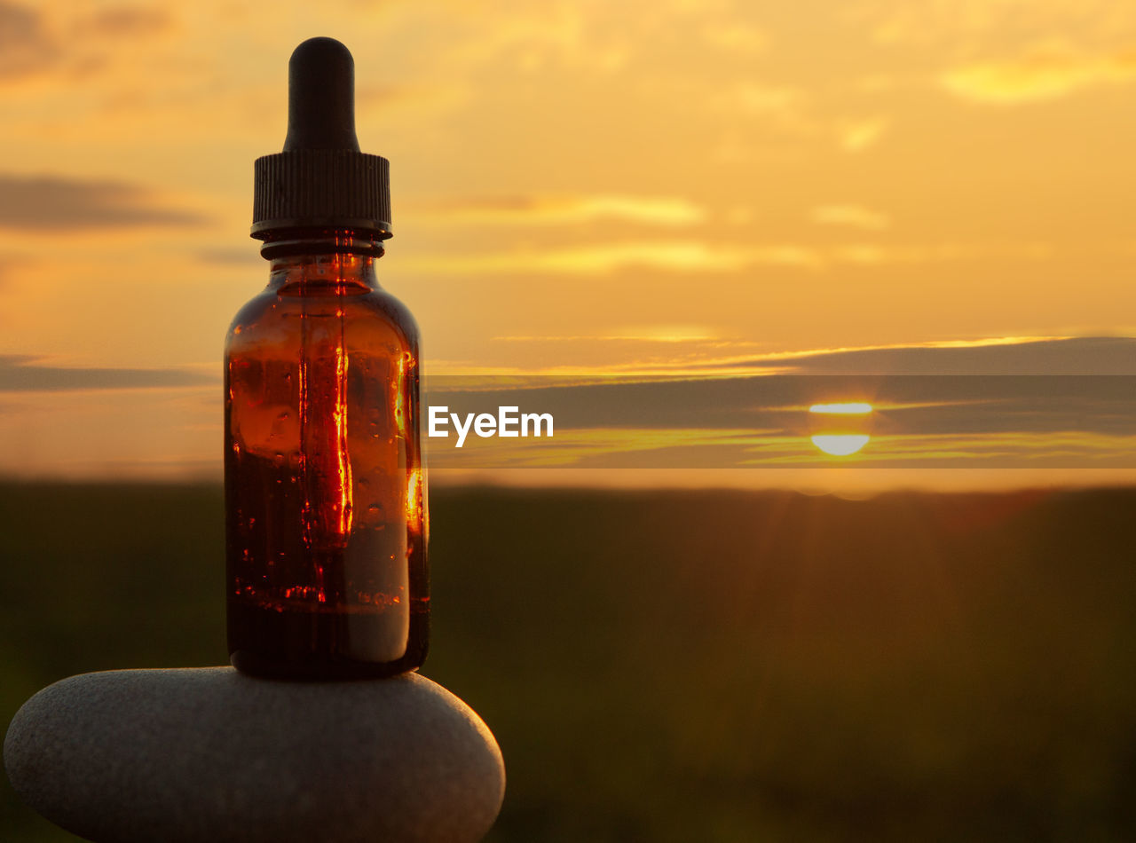 CLOSE-UP OF WATER BOTTLE AGAINST ORANGE SKY