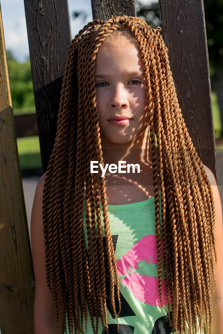 Close-up portrait of girl with dreadlocks standing by wooden fence